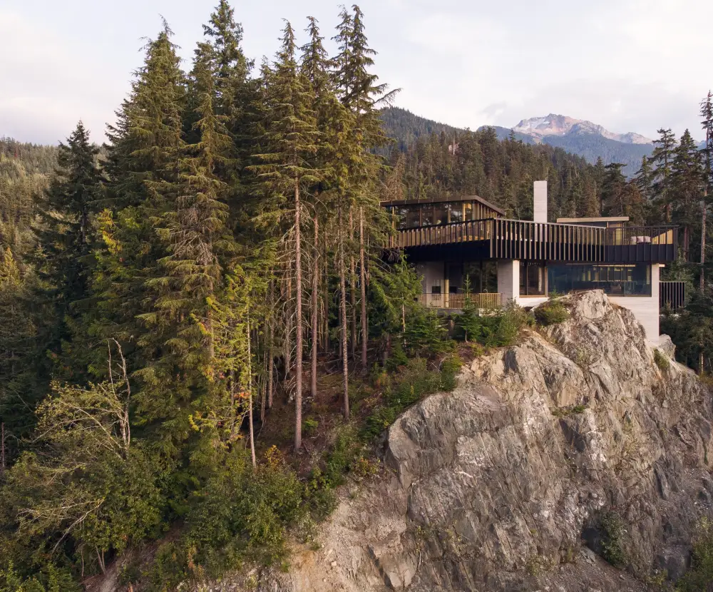 View of dense tall trees and elevation of the house arranged around a rocky outcrop.